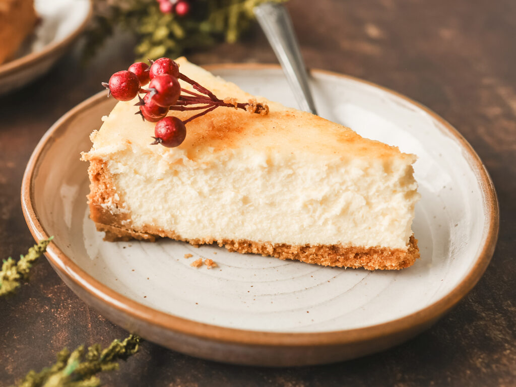 A creamy slice of crème brûlée cheesecake with a golden top, garnished with festive red berries and served on a ceramic plate.