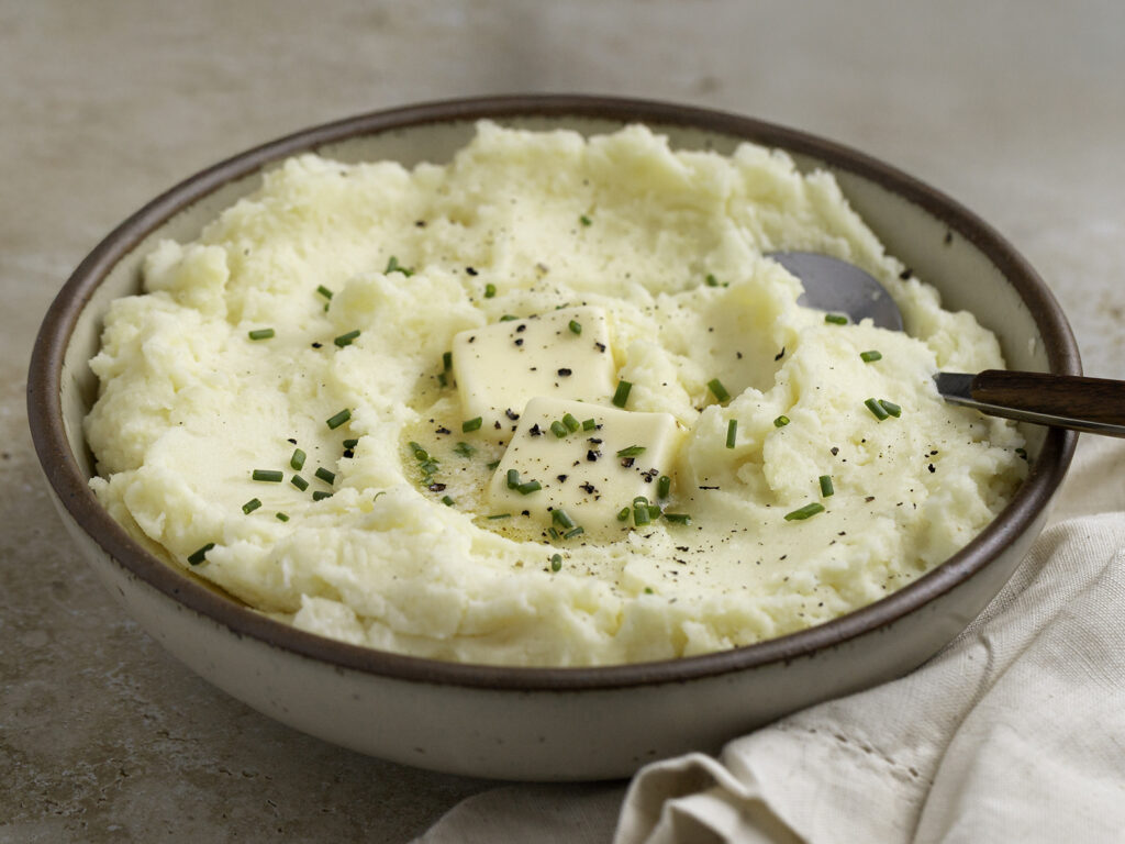 Creamy mashed potatoes served in a rustic bowl, topped with melting butter, chopped chives, and freshly ground black pepper.