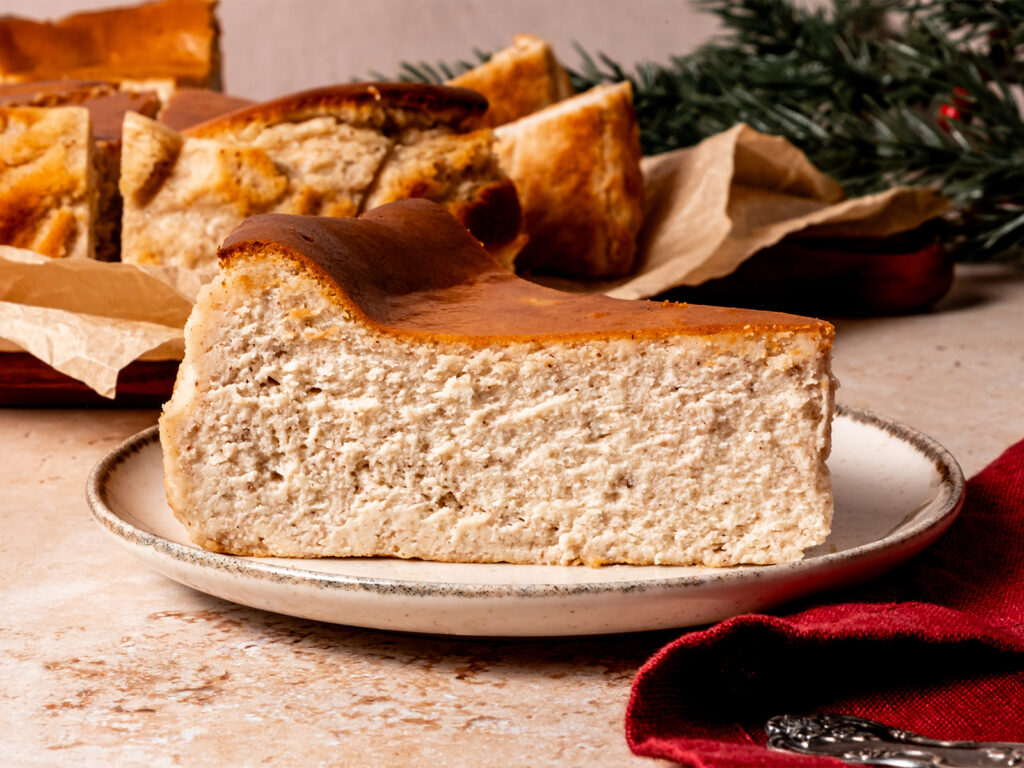A thick slice of gingerbread Basque cheesecake with a golden brown top and creamy, spiced interior on a ceramic plate.