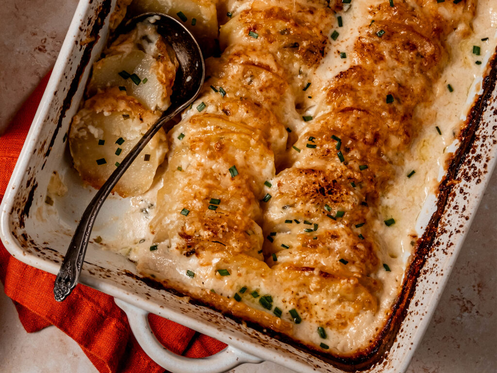 Golden brown sour cream and chive potato gratin baked in a white casserole dish.