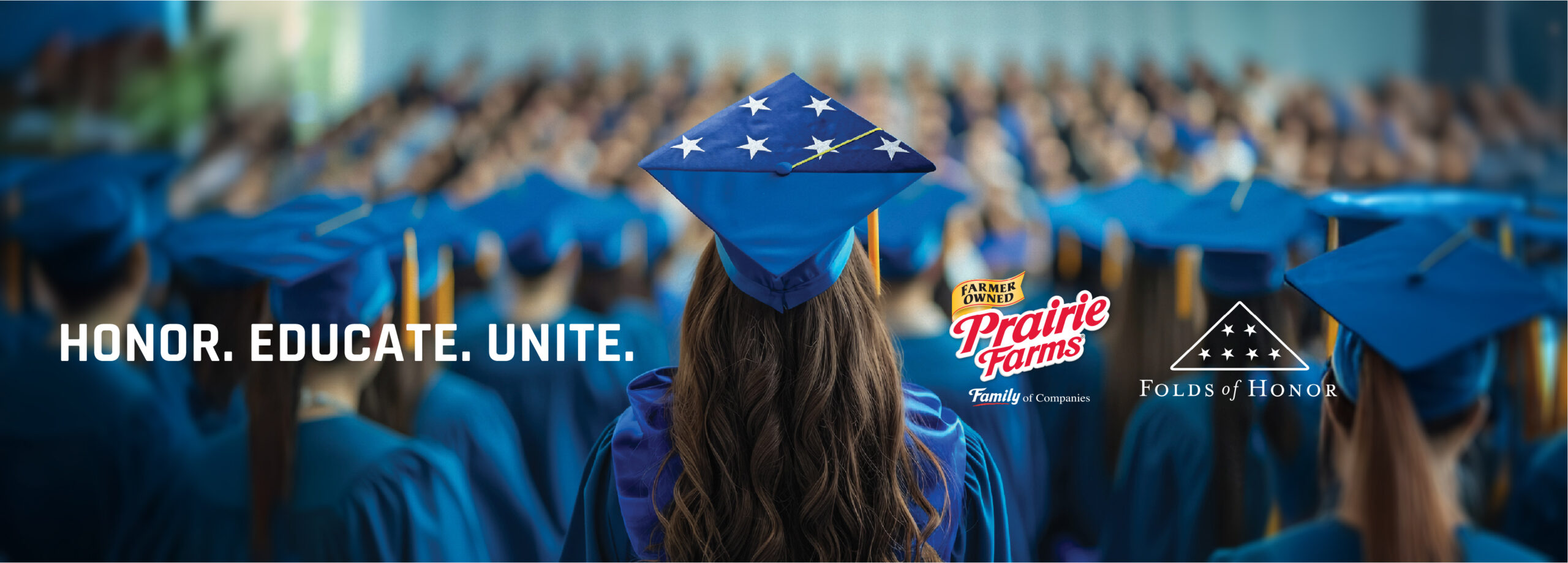 A graduate seen from behind wears a blue cap decorated with white stars while standing among rows of graduates in matching blue gowns at a commencement ceremony. Text over the image reads "Honor Educate Unite" with the Prairie Farms and Folds of Honor logos