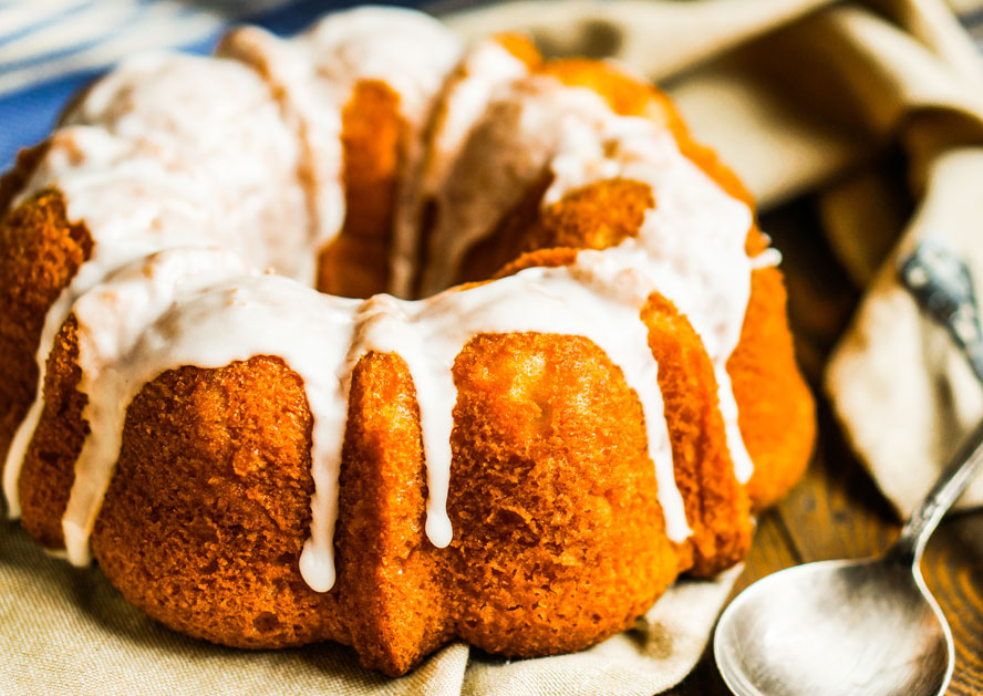 Glazed Bundt cake on a cloth, with a spoon beside it.