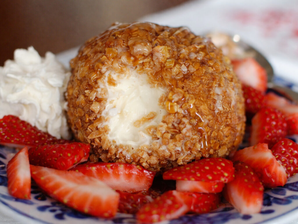 Fried ice cream topped with caramel, served with whipped cream and sliced strawberries.