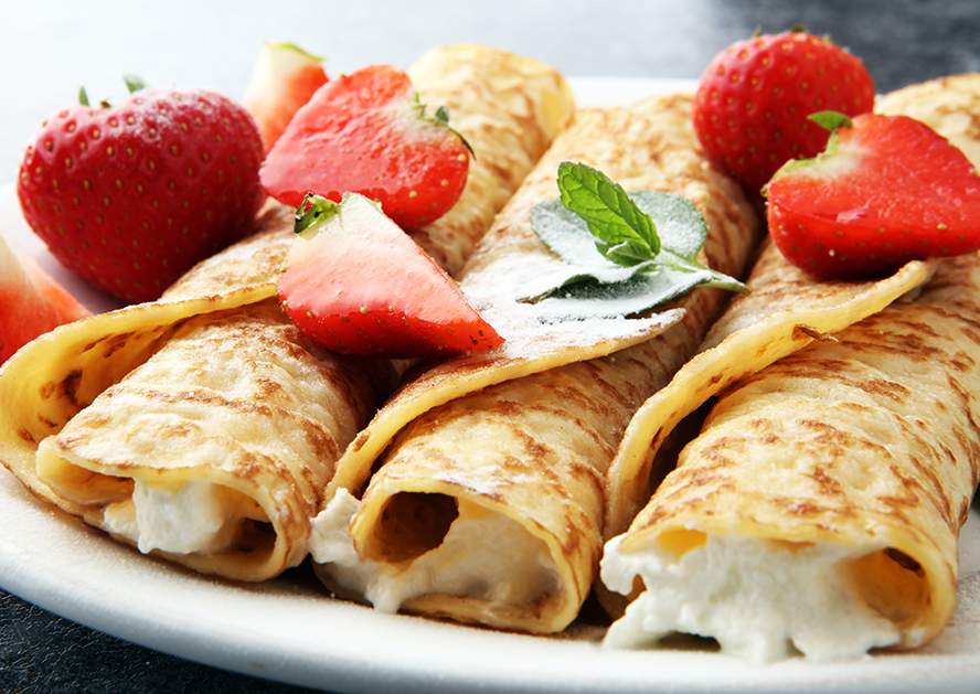 Rolled crepes topped with strawberries and mint on a plate
