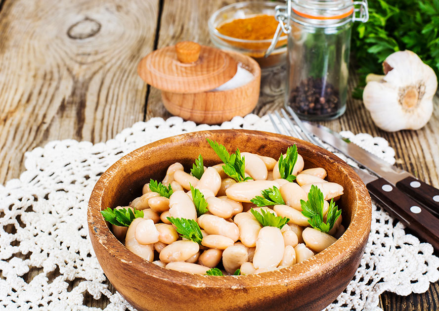 Wooden bowl of white beans garnished with parsley on a rustic table