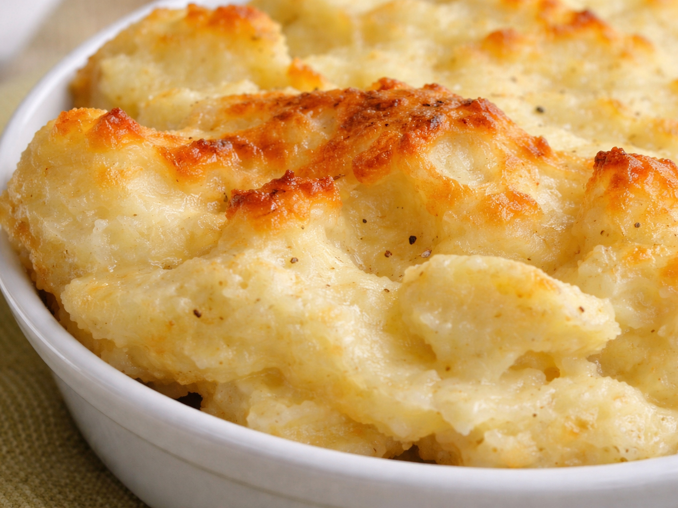 Baked mashed potatoes with browned, melted cheese in a white dish