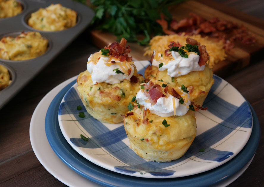 Three loaded potato cups topped with sour cream, bacon, cheese, and chives on a plate