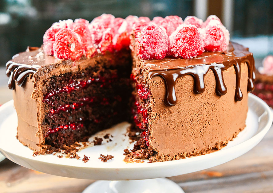 Chocolate layer cake with raspberry filling, chocolate drip frosting, and raspberries on top