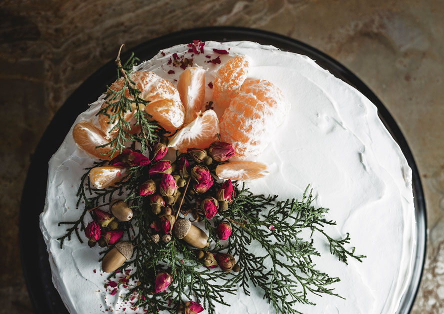 White frosted cake topped with clementine segments, dried flowers, and evergreen sprigs