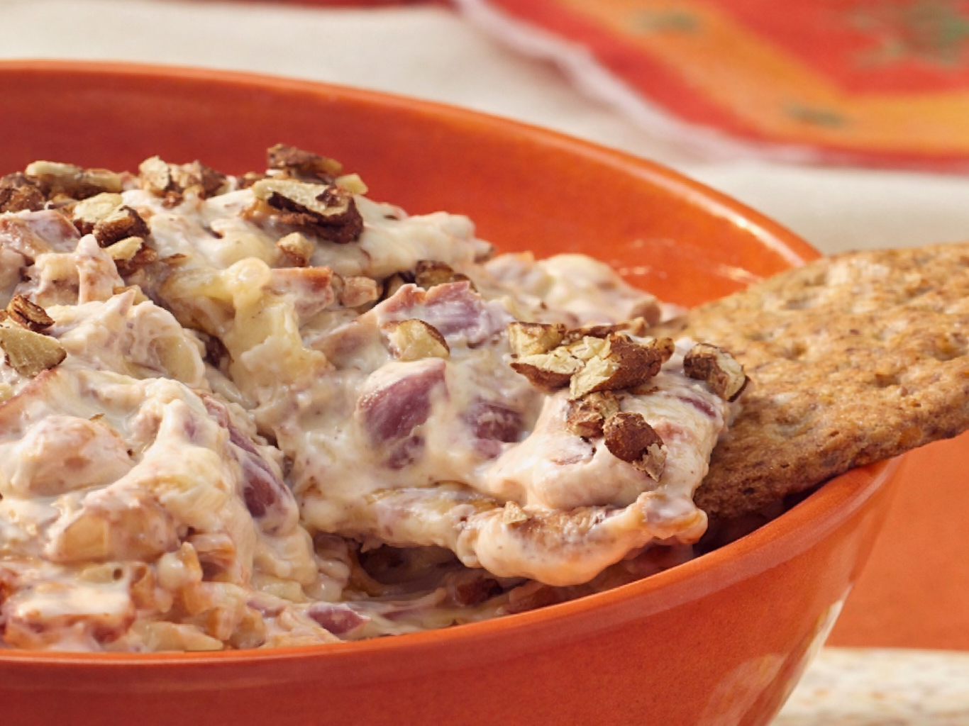 Orange bowl of creamy beef dip topped with chopped meat, served with a cracker.