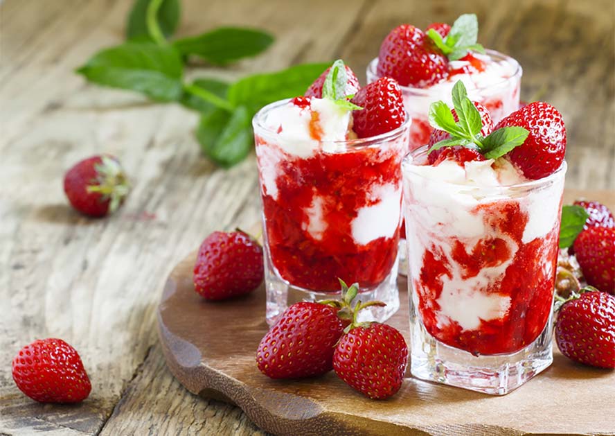 Three glasses of strawberry and whipped cream dessert topped with fresh strawberries and mint