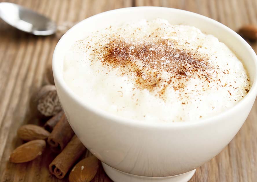 Bowl of rice pudding topped with cinnamon, with cinnamon sticks and almonds beside it