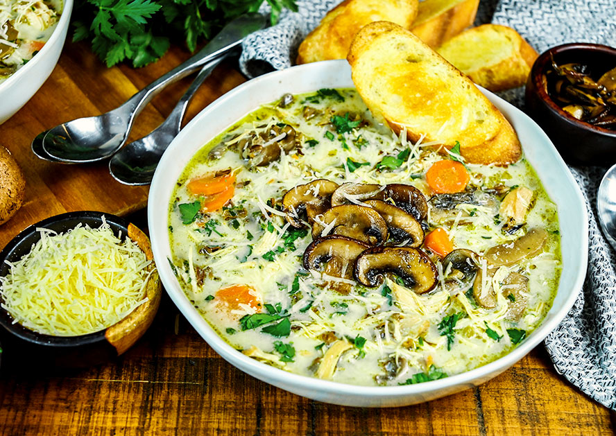 Bowl of mushroom soup topped with herbs and mushrooms, with toasted bread and grated cheese nearby