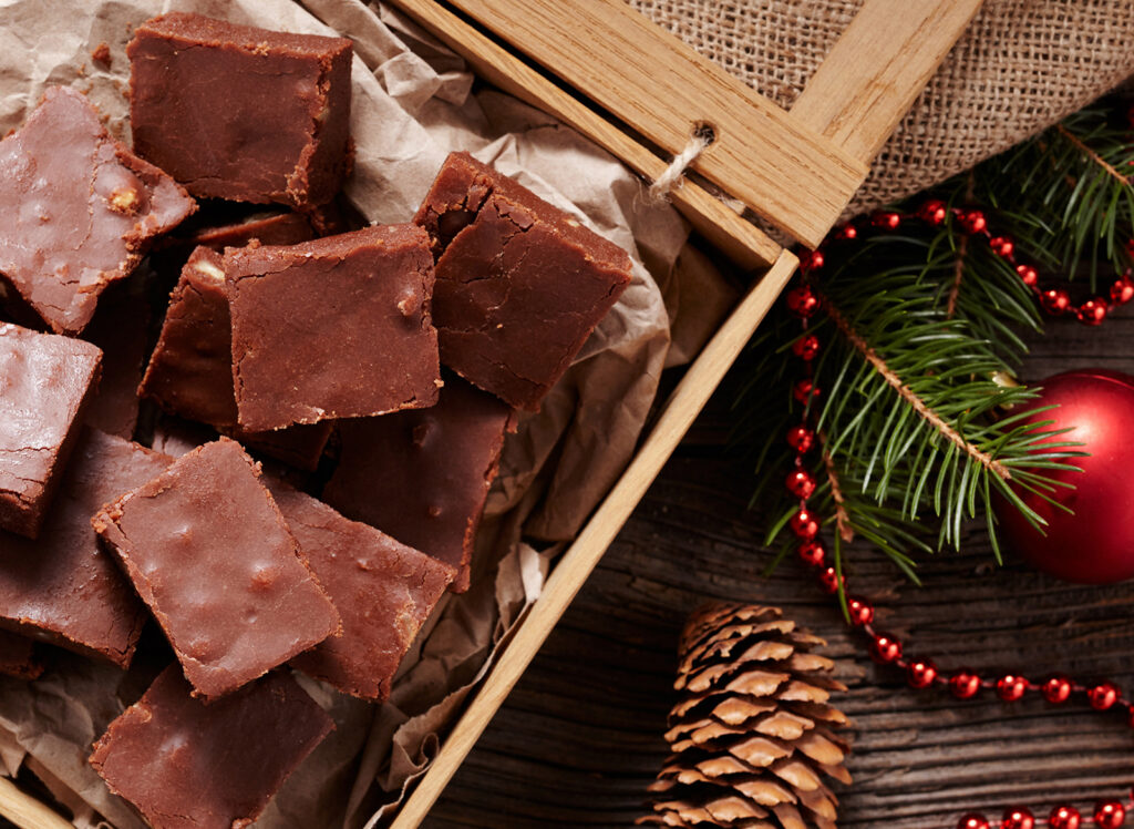 Chocolate fudge squares in a wooden tray with pine branches, ornaments, and a pine cone