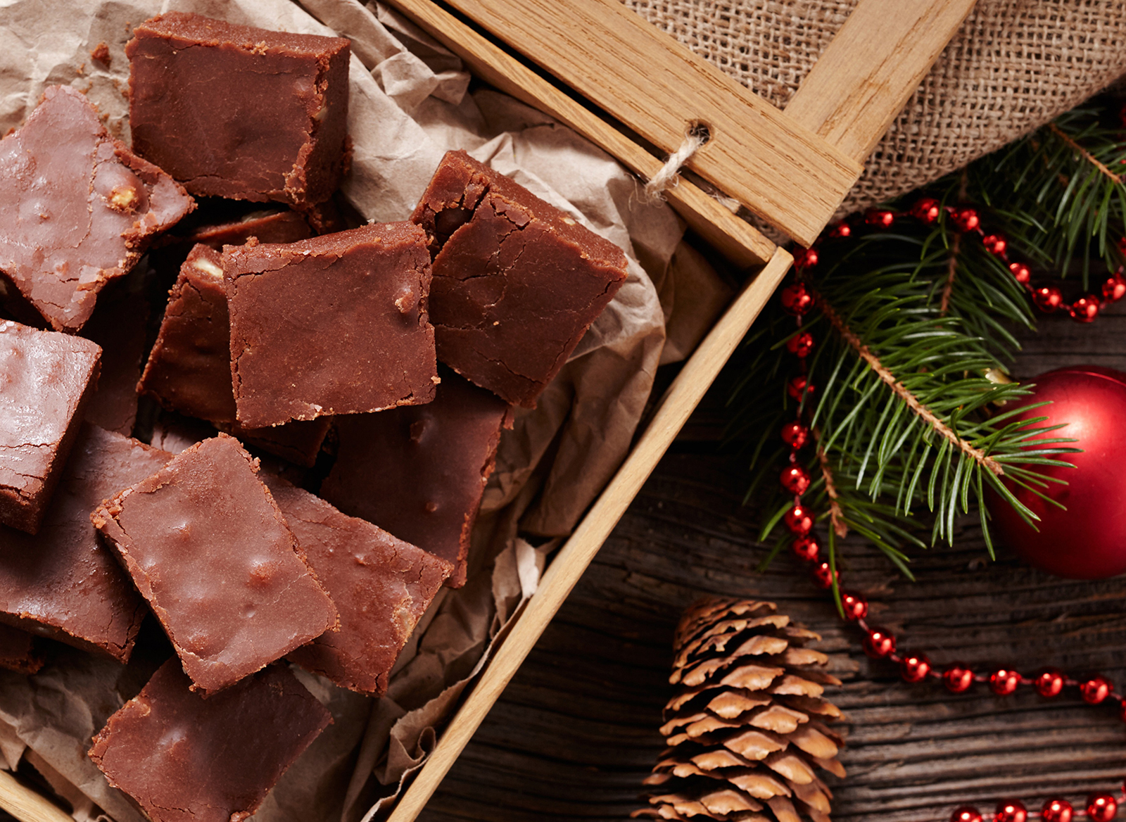Chocolate fudge squares in a wooden tray with pine branches, ornaments, and a pine cone