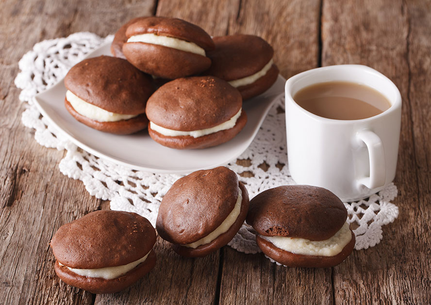 Whoopie pies on a plate and wooden table beside a mug of coffee