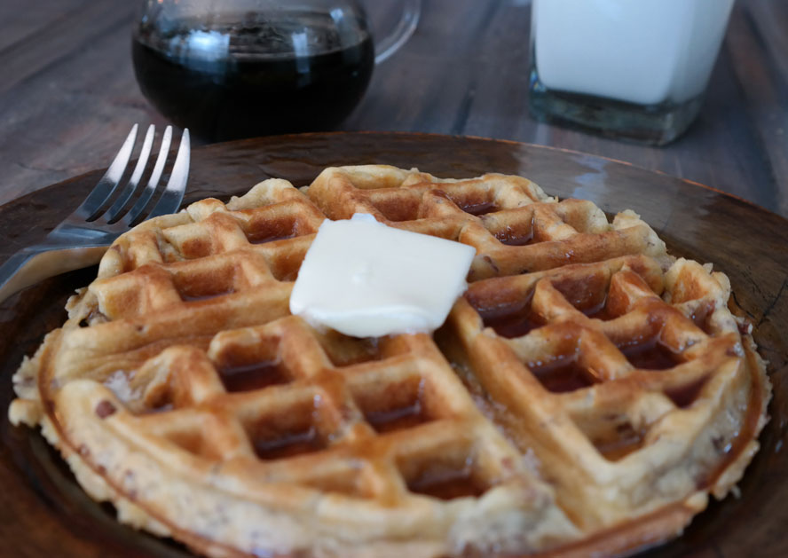 Waffle topped with a pat of butter on a brown plate