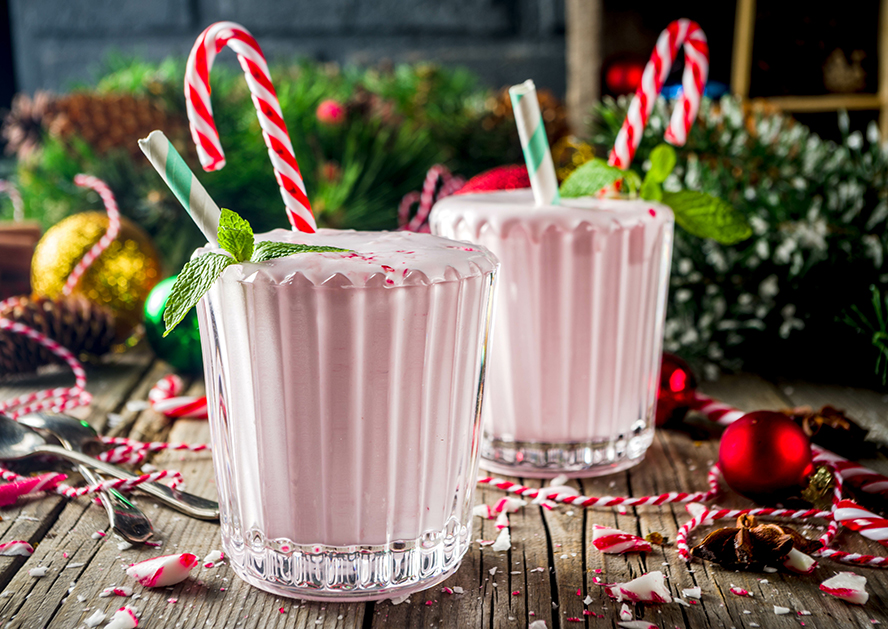 Two pink milkshakes in glasses with peppermint candy canes and mint on a wooden table