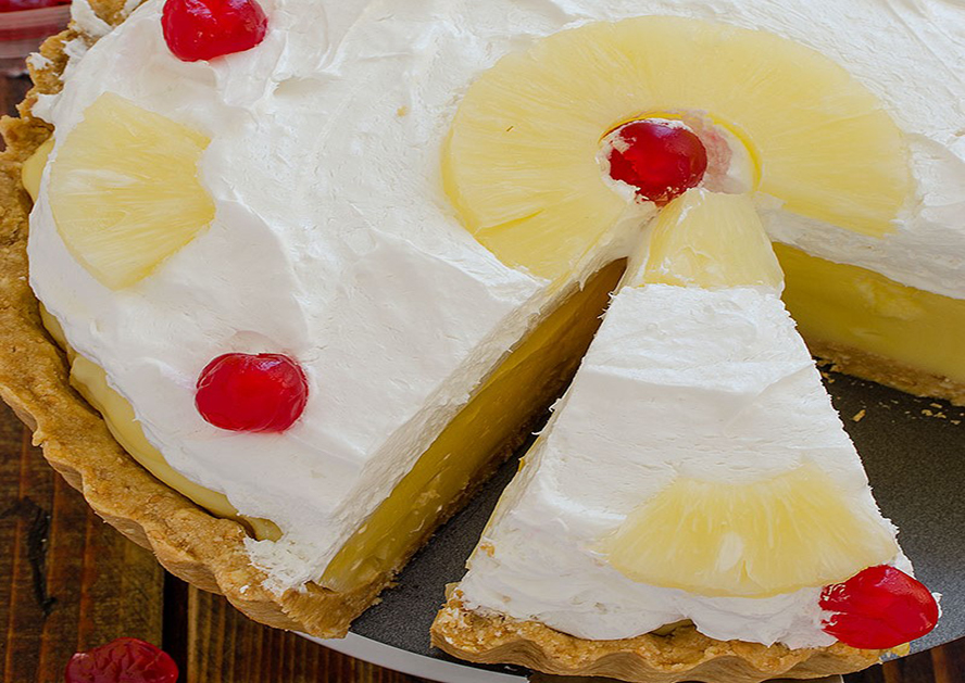 Pineapple pie topped with whipped cream, pineapple slices, and cherries, with a slice cut out