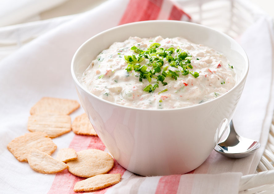 Bowl of creamy dip topped with chopped herbs, with crackers nearby