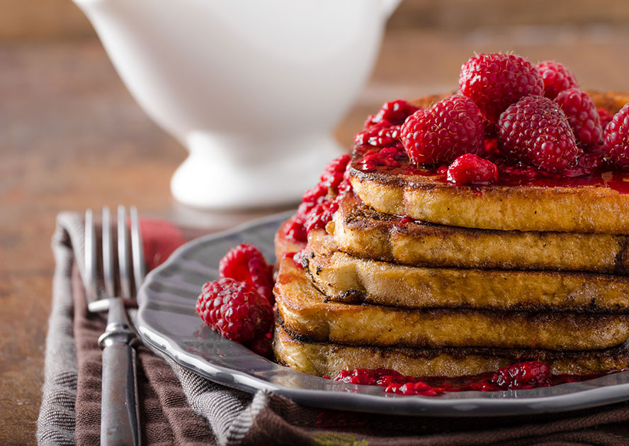 Stack of French toast topped with raspberries and raspberry sauce on a plate