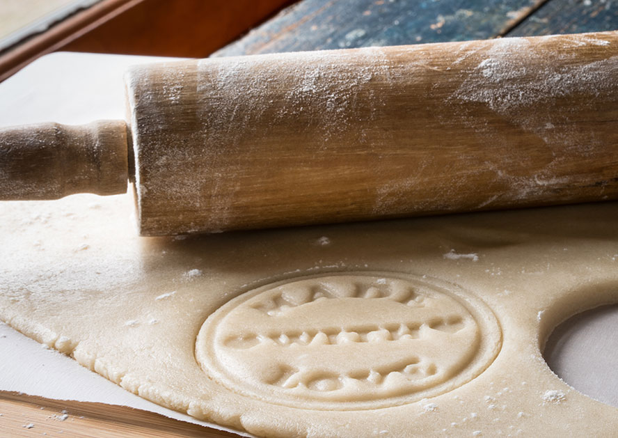 Rolling pin rolling out cookie dough with a decorative stamped design