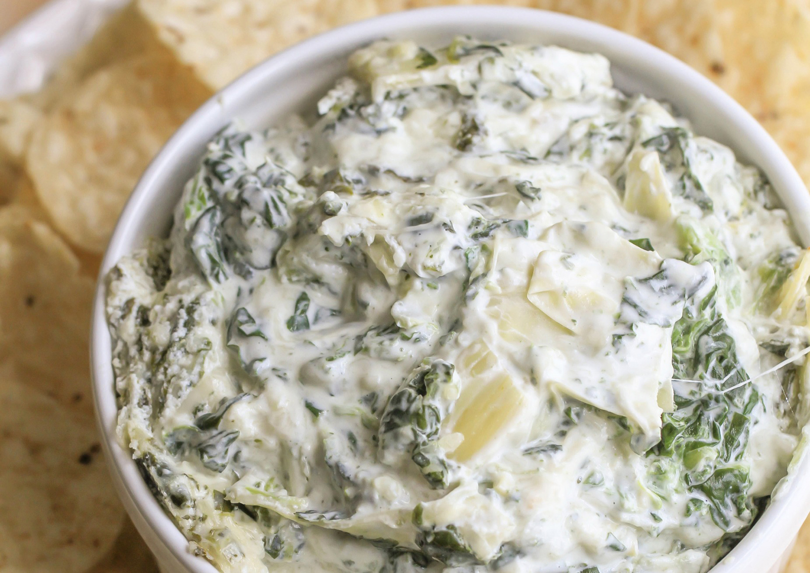 Bowl of spinach artichoke dip with tortilla chips in the background
