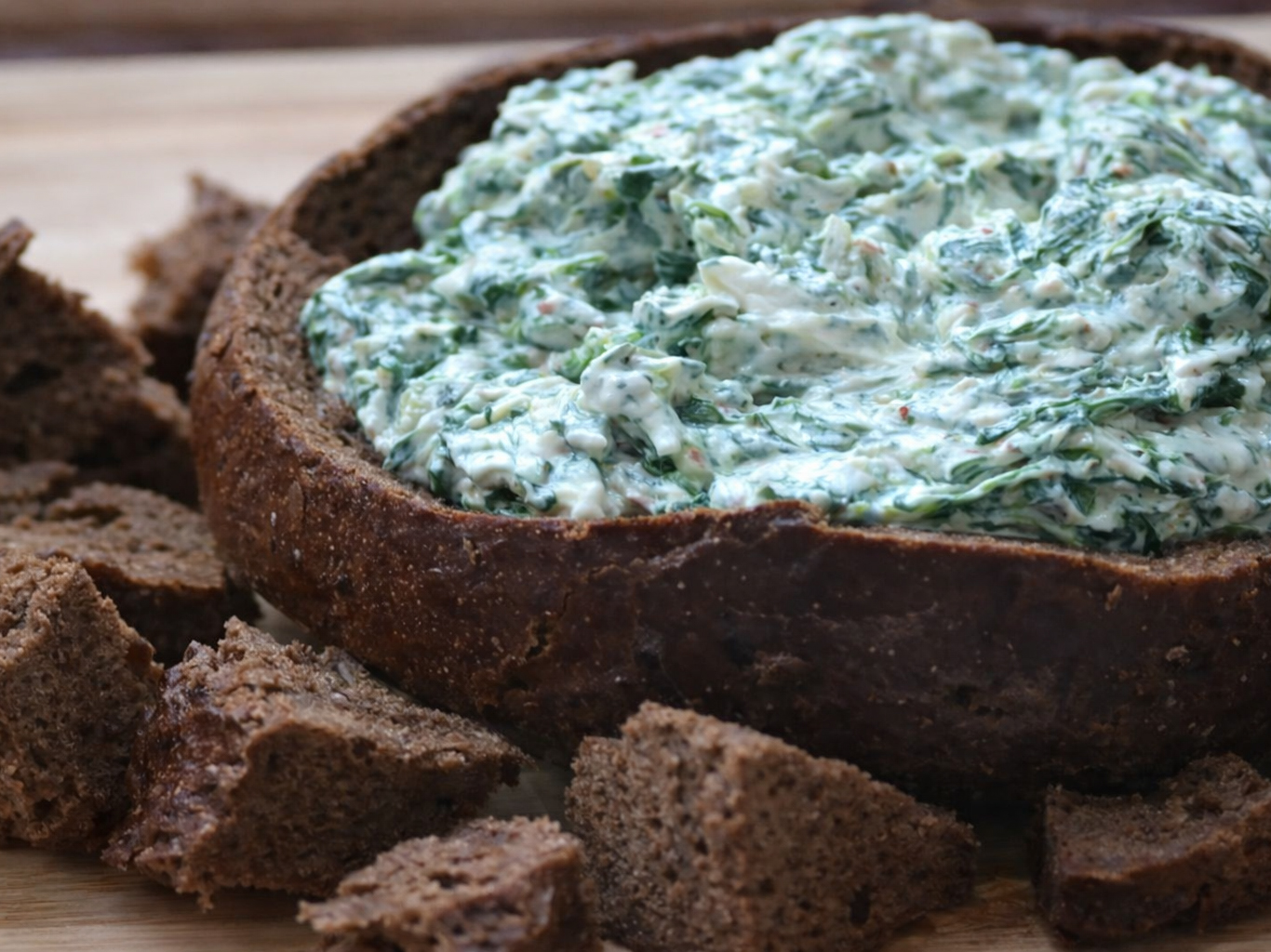 Spinach dip served in a round bread bowl with bread pieces around it