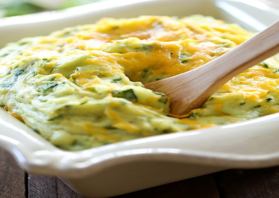 Mashed potatoes mixed with spinach and melted cheese in a white baking dish, with a wooden spoon.