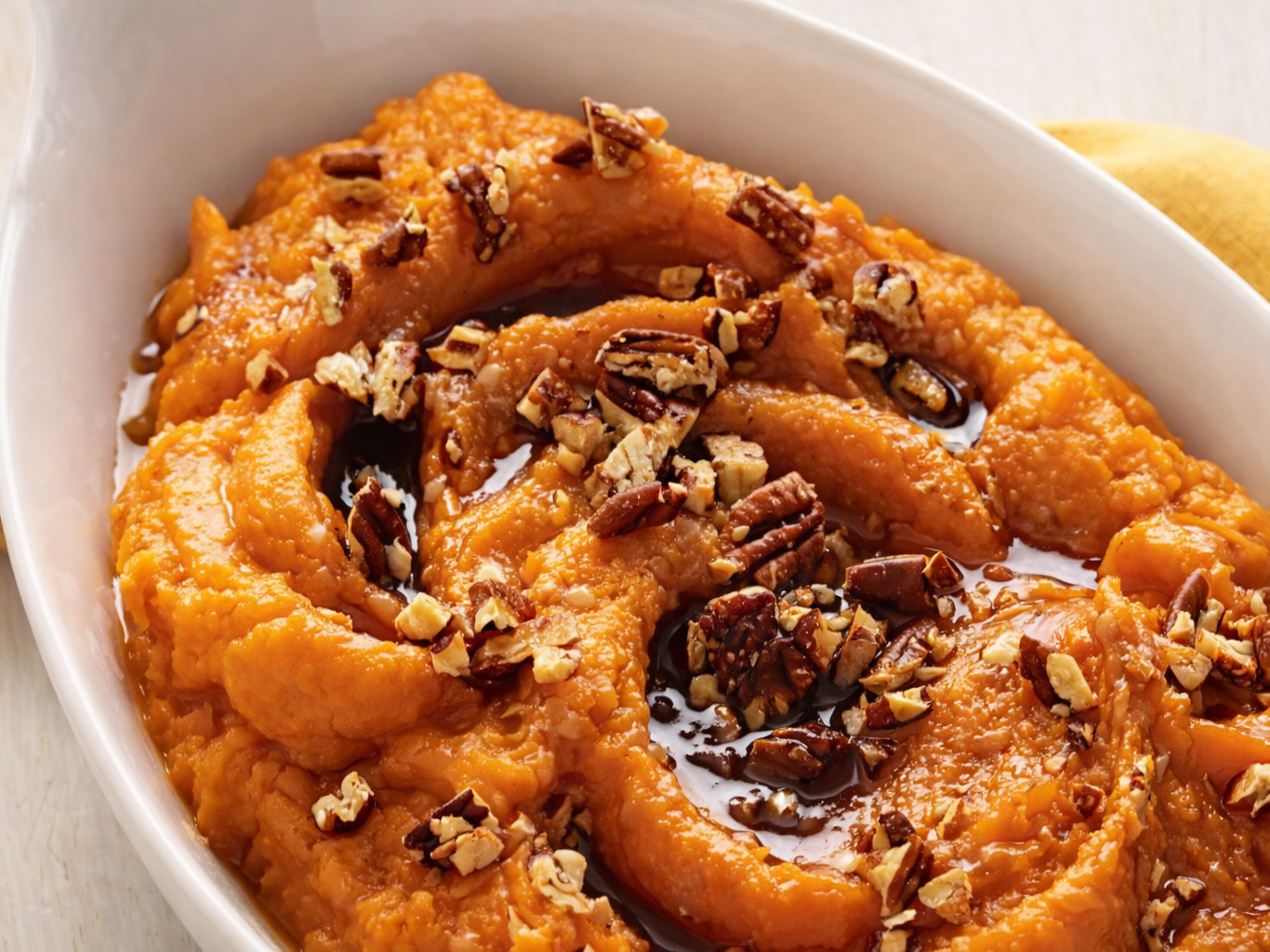 Mashed sweet potatoes topped with chopped hazelnuts and dark syrup in a white bowl.