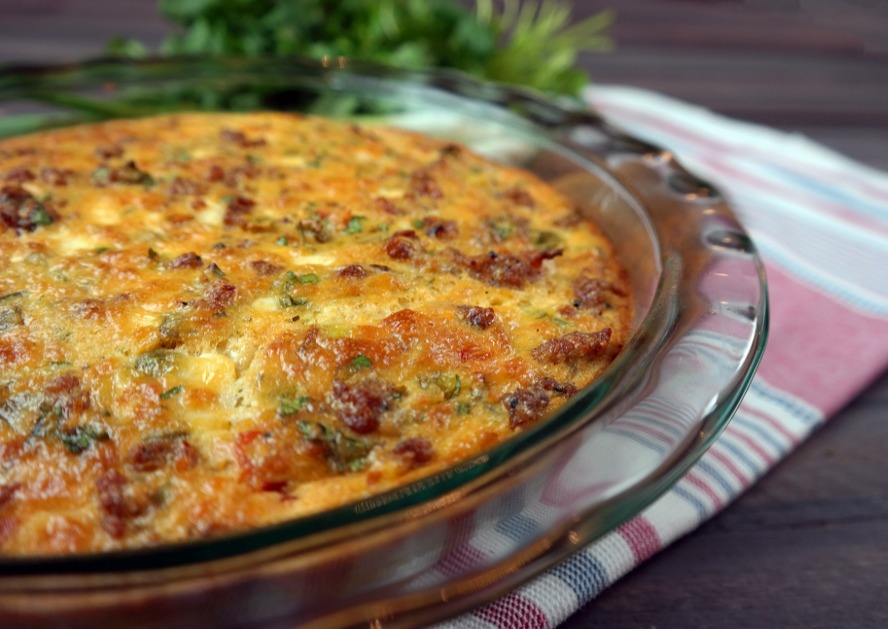 Baked cheesy casserole in a glass pie dish on a striped cloth.