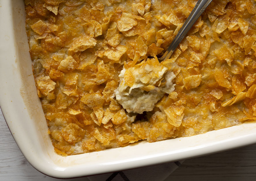 Baked cheesy potato casserole in a white dish with a serving spoon lifting a portion