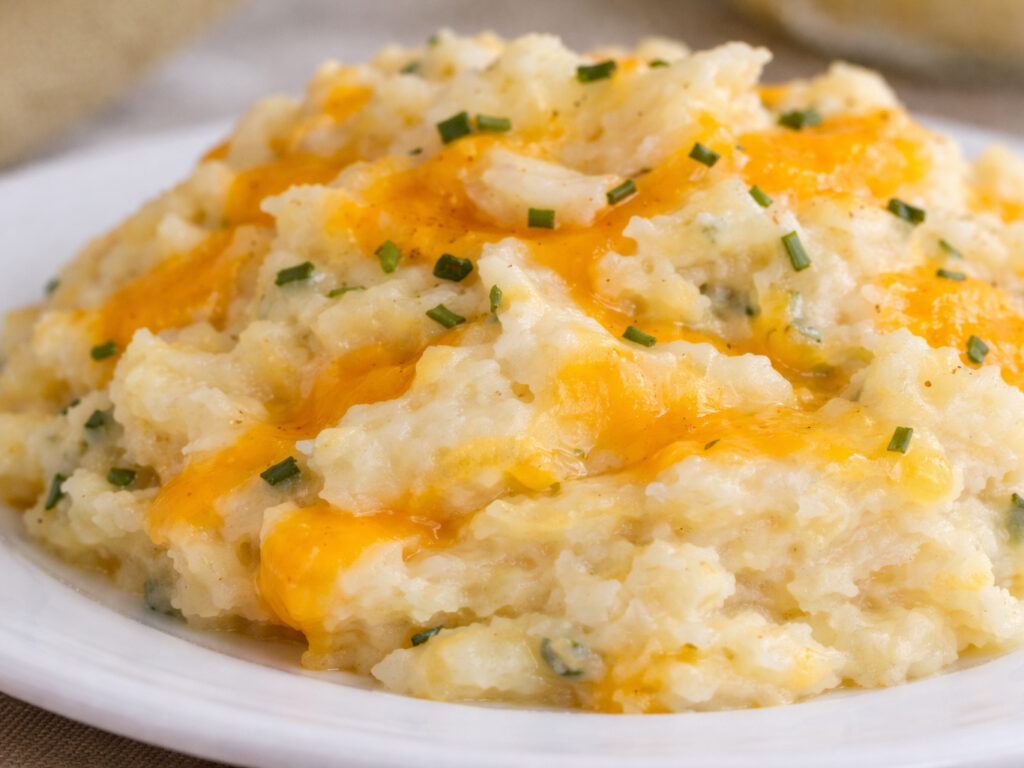 Mashed potatoes topped with melted cheddar and chopped chives on a white plate