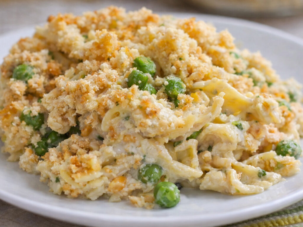 Chicken noodle casserole with peas and a golden crumb topping on a white plate