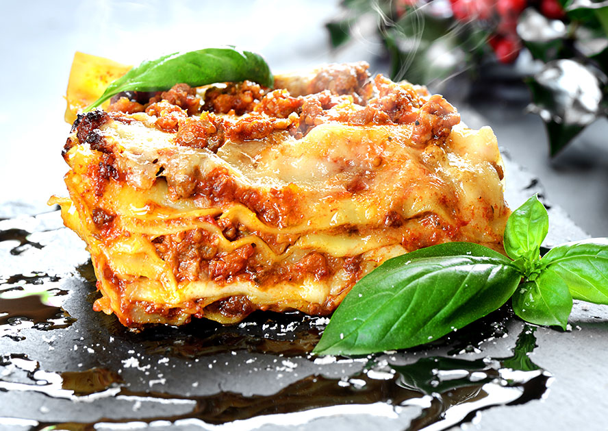 Slice of lasagna topped with meat sauce and basil leaves on a black plate