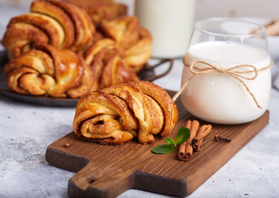 Cinnamon rolls on a wooden board with a glass of milk, cinnamon sticks, and mint.
