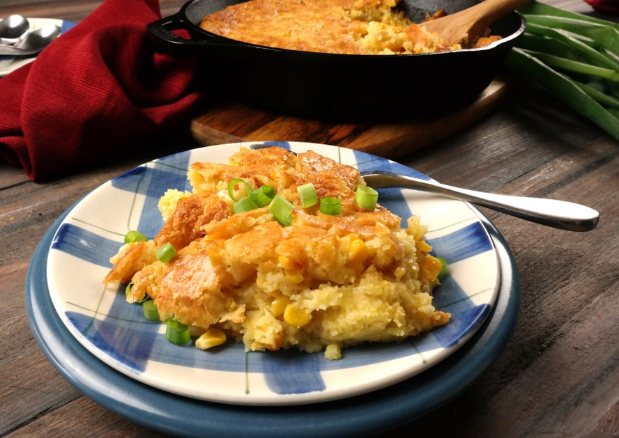 Plate of corn casserole topped with chopped green onions, with a serving spoon nearby.