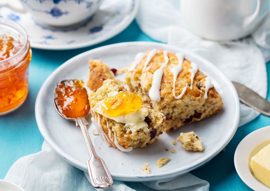 Plate with iced scones, one topped with butter and orange marmalade, beside a spoon and jam jar