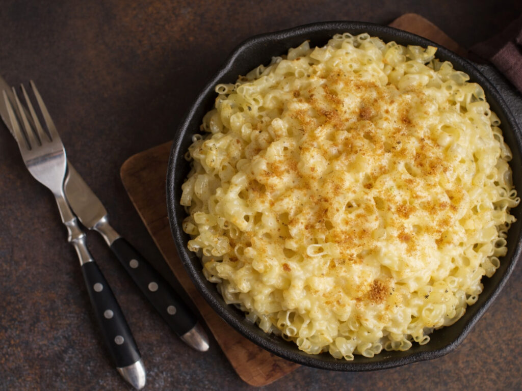 Skillet of baked mac and cheese topped with seasoning, with two forks beside it