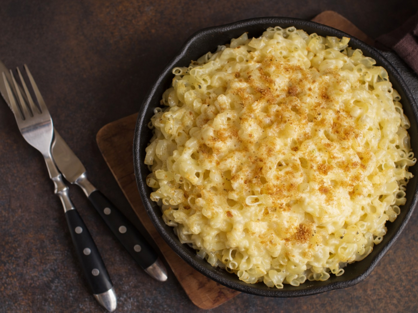Skillet of baked mac and cheese topped with seasoning, with two forks beside it