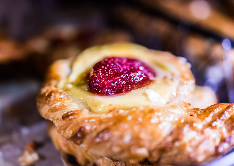Close-up of a glazed pastry topped with cream and a red berry filling.