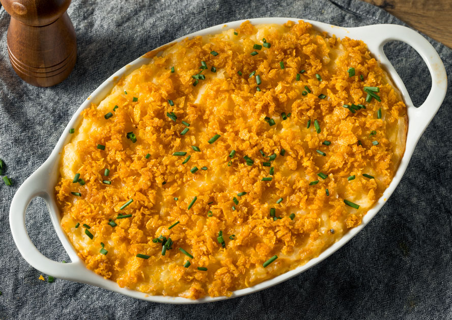 Baked mashed potatoes topped with crushed crackers and chopped chives in an oval white dish