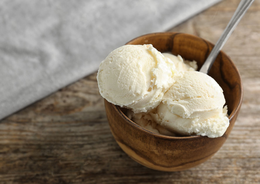 Wooden bowl with two scoops of vanilla ice cream and a spoon