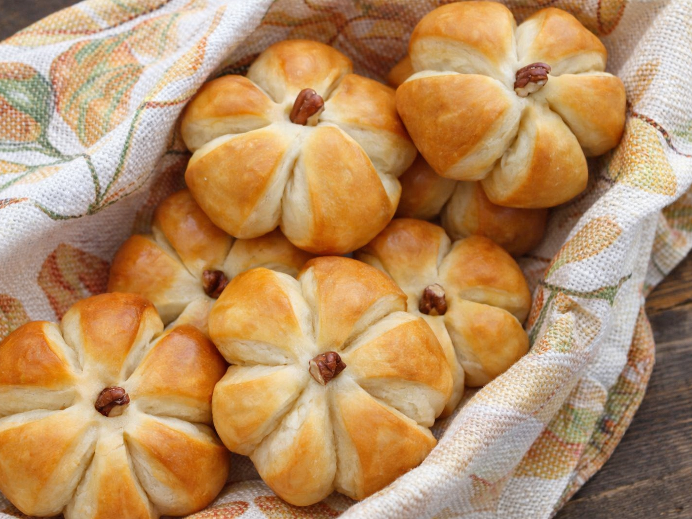 Pumpkin-shaped dinner rolls with pecan stems in a patterned cloth basket