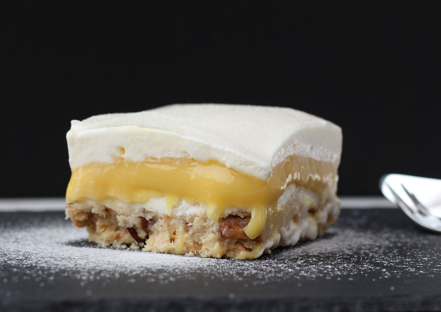 Slice of layered dessert with white cream, yellow custard, and nutty crust