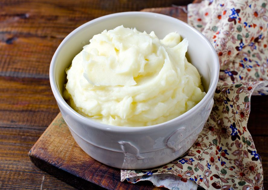 Bowl of mashed potatoes on a wooden board with a floral cloth.
