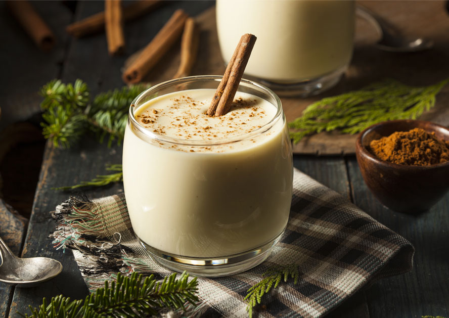 Glass of eggnog topped with a cinnamon stick on a plaid cloth