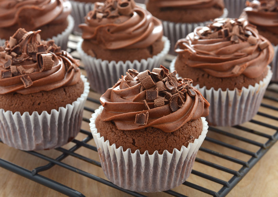 Chocolate cupcakes with swirled frosting and chocolate shavings on a cooling rack