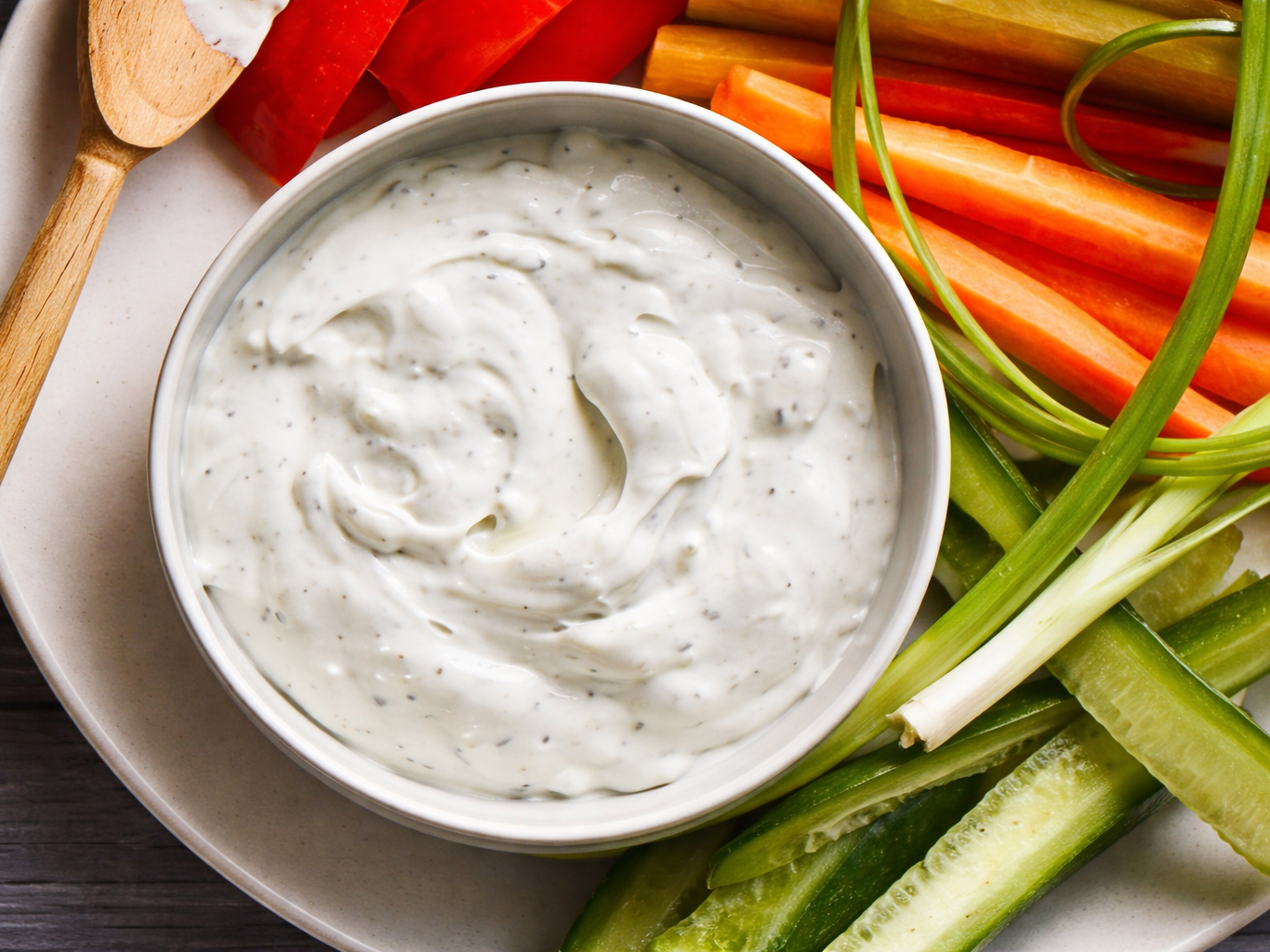 Bowl of creamy herb dip with sliced carrots, celery, and cucumber on a plate
