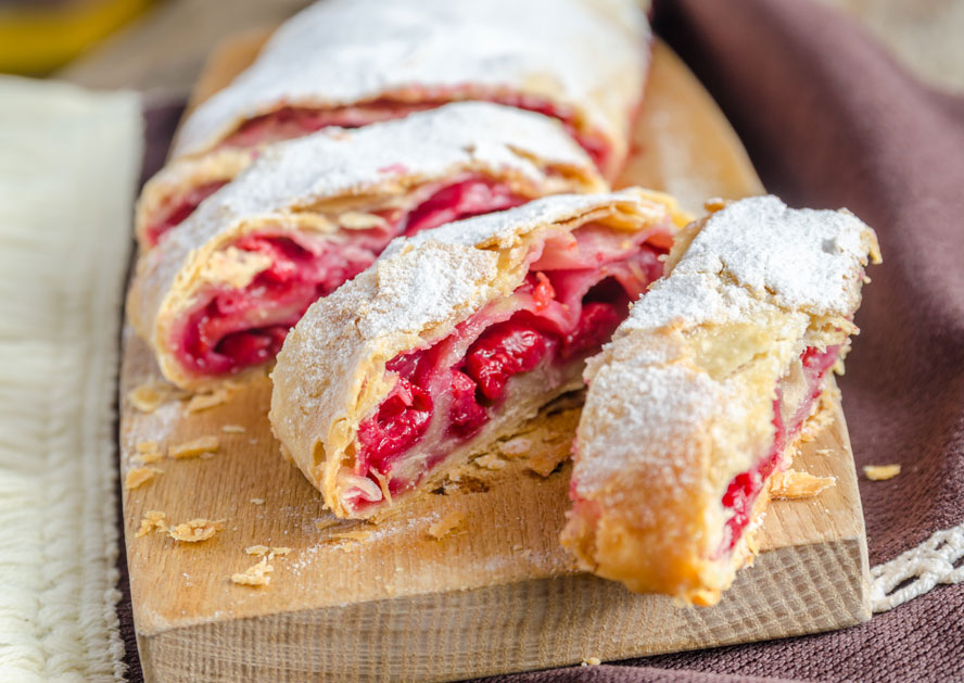 Sliced raspberry strudel dusted with powdered sugar on a wooden board